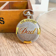 A decorative silver globe pendant with intricate engravings, displayed on a beige surface alongside a brown cord.